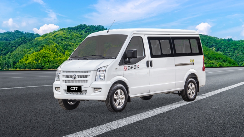 Vista delantera lateral de van de turismo DFSK C37 X9 color blanca en autopista con fondo de montañas.
